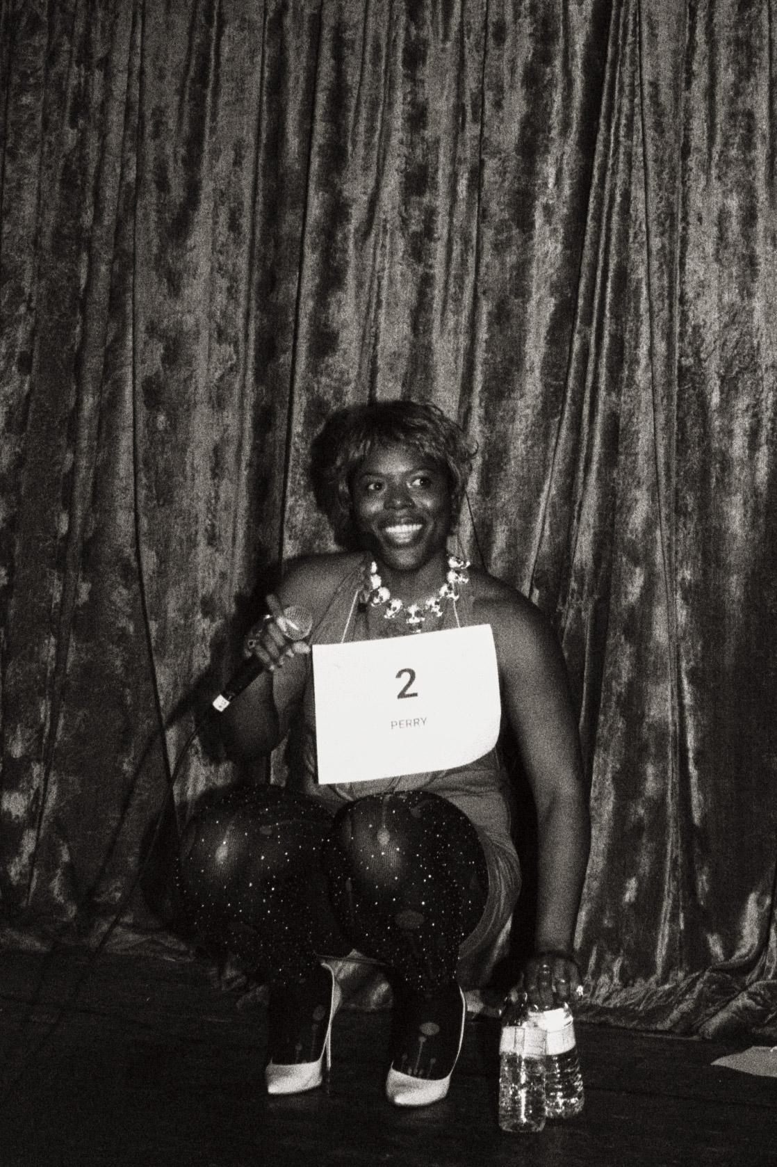 Fraud Perry smiles onstage while holding a microphone and wearing contestant number two